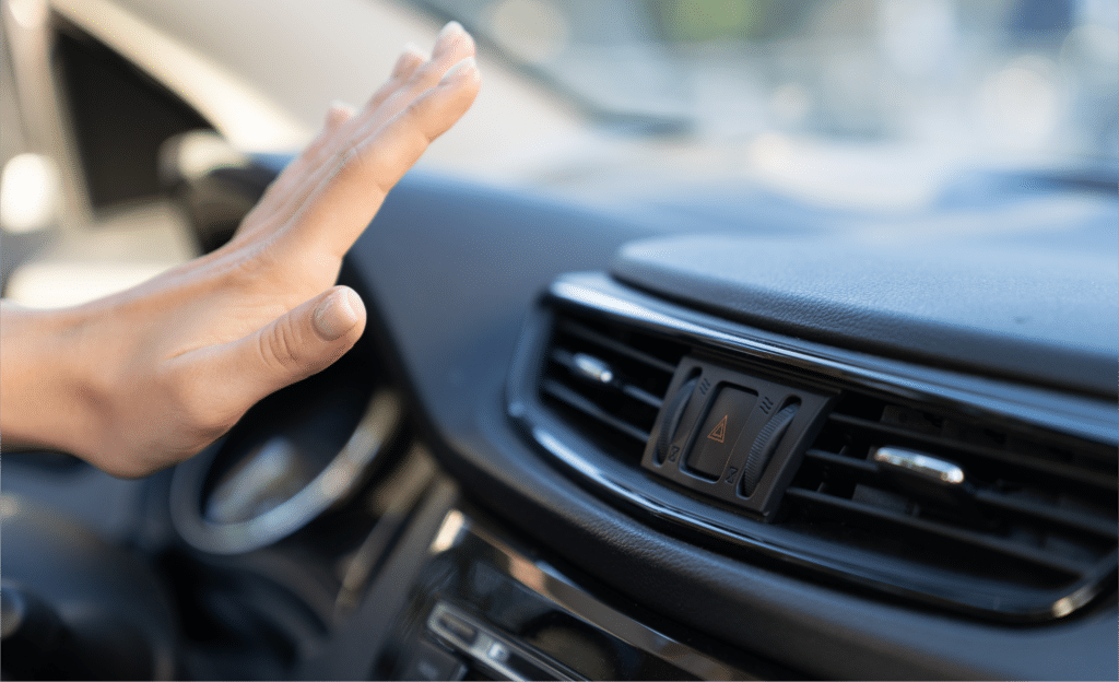 A hand reaching towards an air vent on a car dashboard at Horeb Auto Repair, with the hazard light button visible between the air vents.