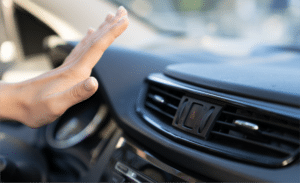A hand reaching towards an air vent on a car dashboard at Horeb Auto Repair, with the hazard light button visible between the air vents.