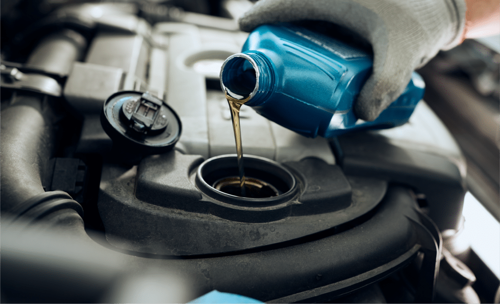 At Horeb Auto Repair, a person wearing gloves carefully pours motor oil from a blue bottle into a car engine.