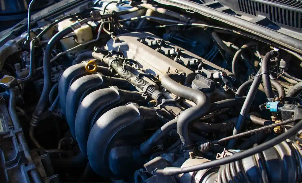 Close-up of a car engine with visible manifolds, hoses, and a yellow oil dipstick.